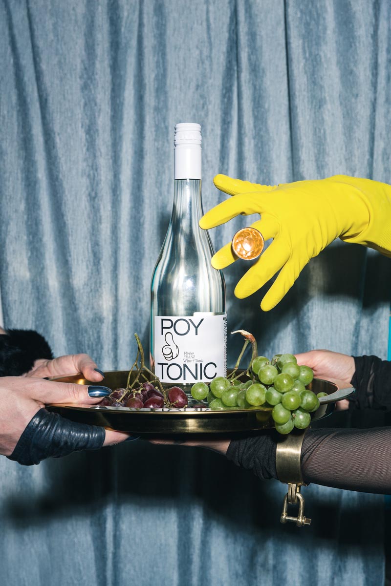 Eine Flasche des Getränks Poytonic bei einem Fotoshooting mit Werbefotograf Clemens Schneider vor blauem Vorhang und Weintrauben
